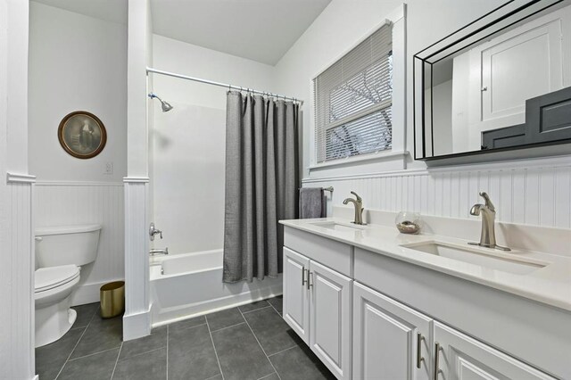 bathroom with toilet, a sink, tile patterned flooring, and a wainscoted wall