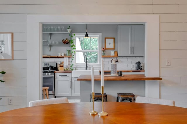 kitchen with decorative backsplash, decorative light fixtures, stainless steel gas range oven, open shelves, and a sink
