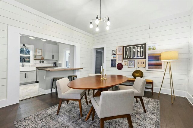 dining room featuring wooden walls, a notable chandelier, and dark wood-type flooring