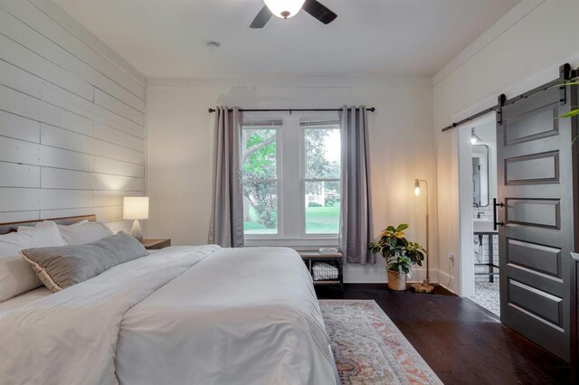 bedroom featuring wooden walls, a ceiling fan, a barn door, and dark wood-type flooring