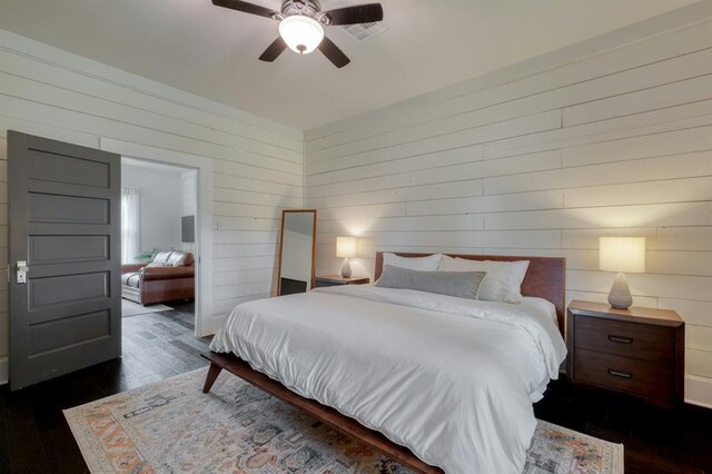 bedroom featuring a ceiling fan, wood walls, dark wood finished floors, and visible vents