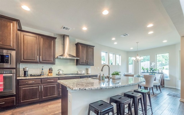kitchen featuring a sink, stainless steel appliances, wall chimney exhaust hood, and visible vents
