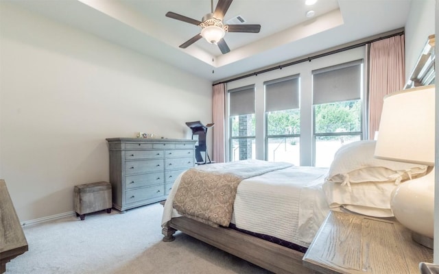 bedroom featuring light colored carpet, a ceiling fan, baseboards, a tray ceiling, and visible vents