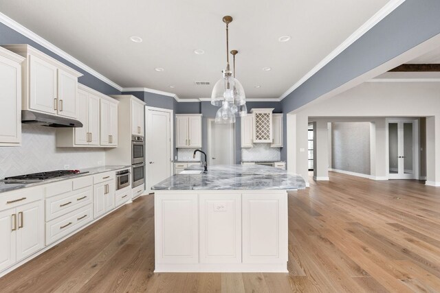 kitchen featuring a center island with sink, backsplash, under cabinet range hood, and light stone countertops
