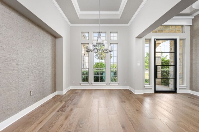 unfurnished dining area with wood finished floors, baseboards, a raised ceiling, a chandelier, and ornamental molding