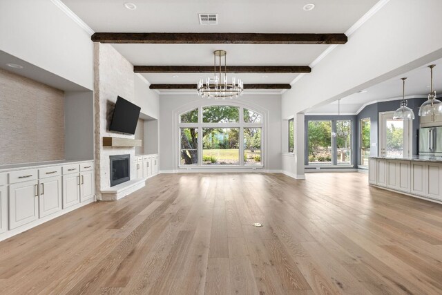 unfurnished living room with an inviting chandelier, plenty of natural light, a large fireplace, light wood-type flooring, and visible vents