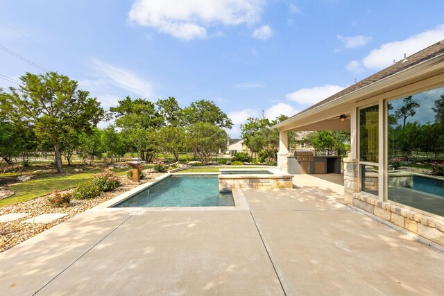 view of swimming pool featuring a patio, a pool with connected hot tub, and exterior kitchen