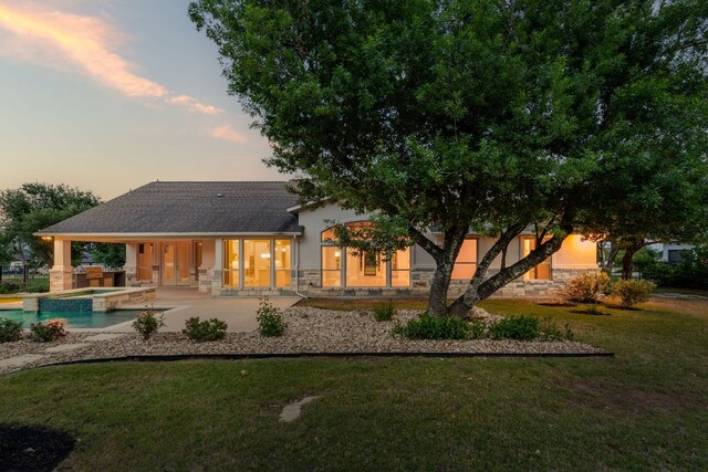 back of house featuring a yard, stone siding, a patio area, and stucco siding