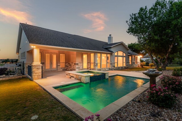 back of property at dusk featuring french doors, a chimney, a patio, a shingled roof, and stone siding