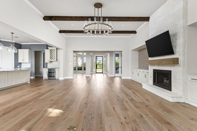 unfurnished living room with a notable chandelier, beam ceiling, light wood-style floors, a fireplace, and beverage cooler