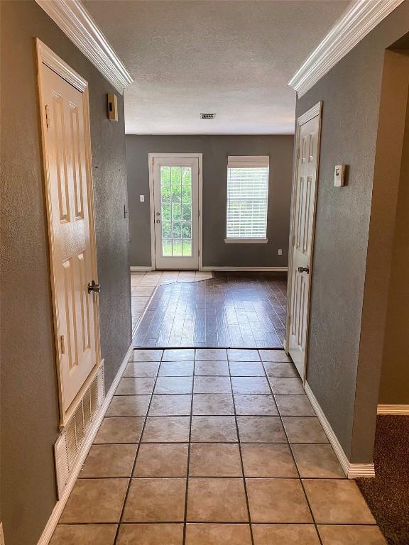 hallway featuring baseboards, a textured wall, ornamental molding, and visible vents