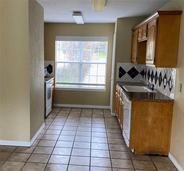 kitchen featuring dark countertops, a sink, light tile patterned floors, backsplash, and dishwashing machine