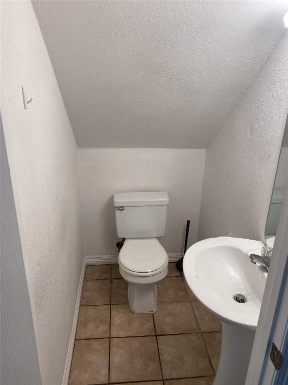 bathroom featuring a sink, toilet, a textured ceiling, tile patterned floors, and baseboards