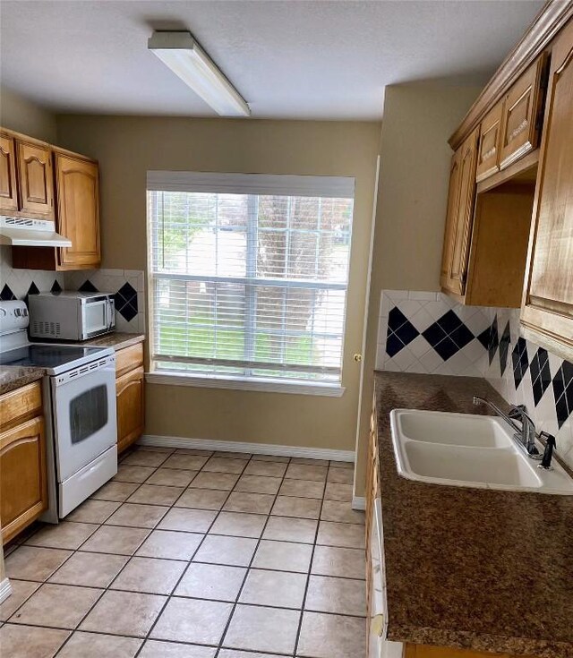 kitchen featuring dark countertops, tasteful backsplash, a sink, under cabinet range hood, and white appliances