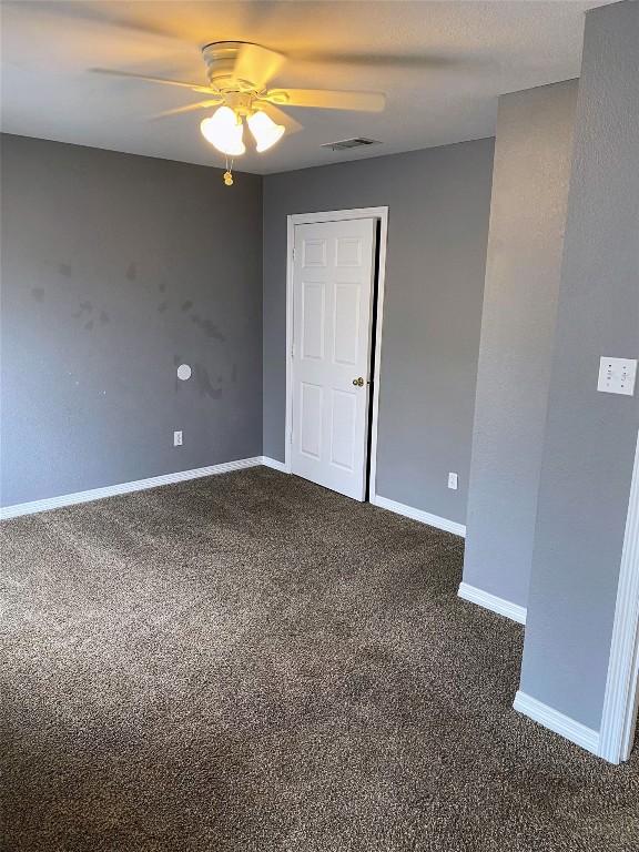 unfurnished room featuring visible vents, a ceiling fan, baseboards, and dark carpet