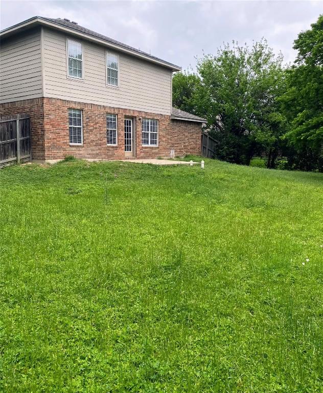 rear view of property featuring brick siding, a lawn, and fence