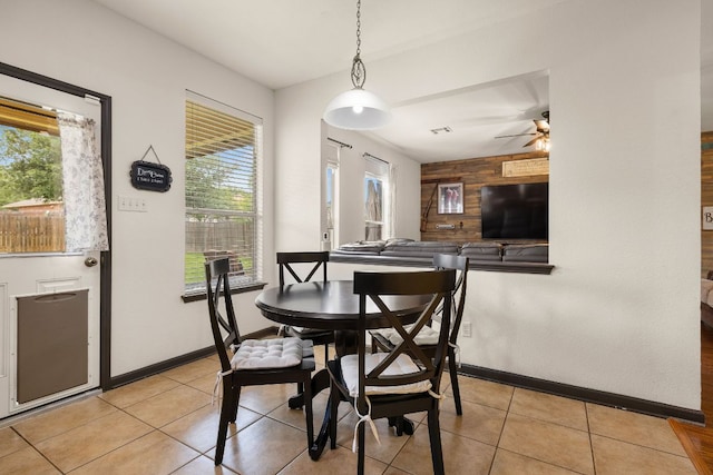 dining space featuring wooden walls, a ceiling fan, light tile patterned flooring, and a wealth of natural light