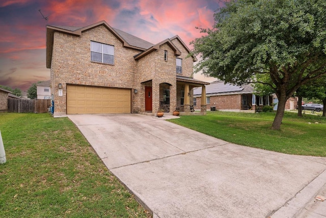 traditional-style home featuring a garage, fence, brick siding, concrete driveway, and a yard