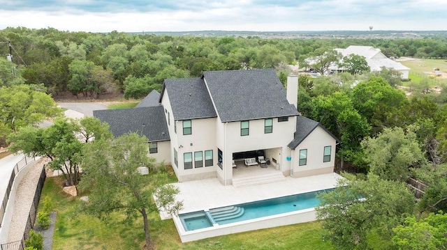 rear view of house featuring a shingled roof, stucco siding, an outdoor pool, a chimney, and a patio
