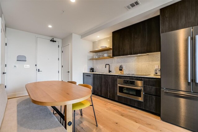 kitchen featuring dark brown cabinetry, light wood finished floors, stainless steel appliances, backsplash, and visible vents