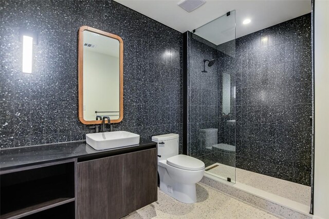 full bathroom featuring vanity, visible vents, toilet, tiled shower, and speckled floor