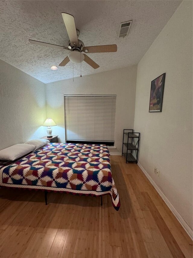 bedroom with a textured ceiling, visible vents, lofted ceiling, and hardwood / wood-style flooring