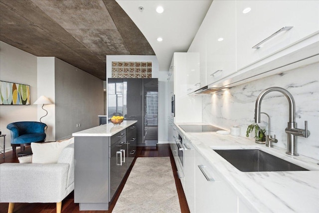 kitchen featuring wood finished floors, light stone countertops, black electric stovetop, white cabinets, and a sink