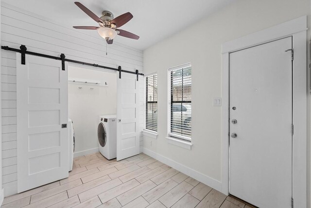 laundry area with ceiling fan, a barn door, baseboards, light wood-type flooring, and washer and clothes dryer