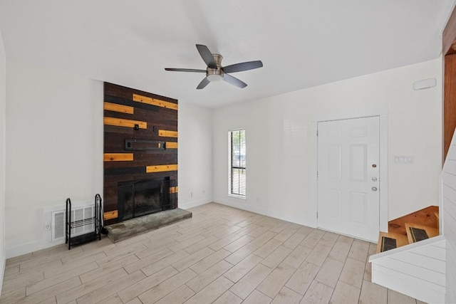 unfurnished living room featuring a ceiling fan, baseboards, a fireplace with raised hearth, light wood finished floors, and stairs
