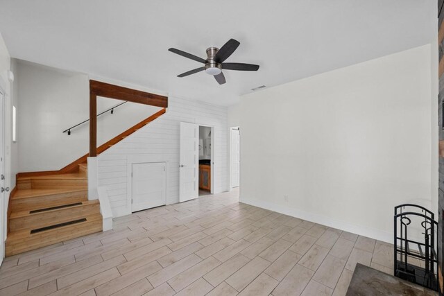 unfurnished living room featuring ceiling fan, baseboards, wood finished floors, visible vents, and stairway
