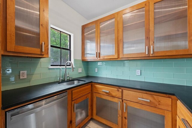 kitchen featuring stainless steel dishwasher, dark countertops, brown cabinetry, and a sink