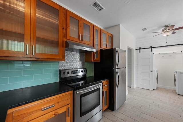 kitchen with visible vents, washer and dryer, a barn door, under cabinet range hood, and stainless steel appliances