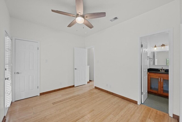unfurnished bedroom featuring visible vents, a sink, baseboards, light wood finished floors, and ensuite bathroom