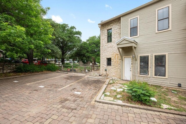 view of front facade featuring uncovered parking, fence, and stone siding