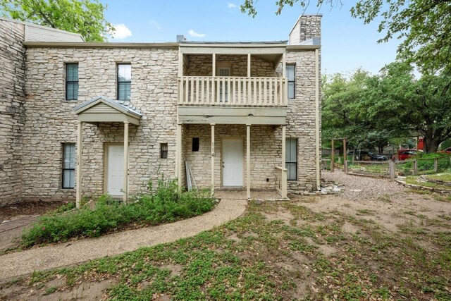 view of front of house with a chimney, fence, a balcony, and stone siding