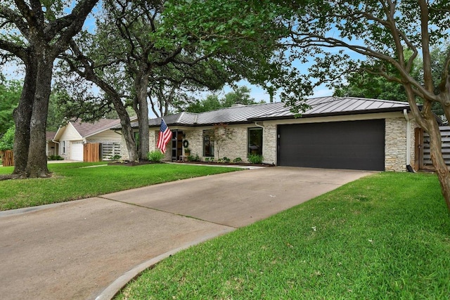 ranch-style house featuring a standing seam roof, a front lawn, concrete driveway, an attached garage, and stone siding