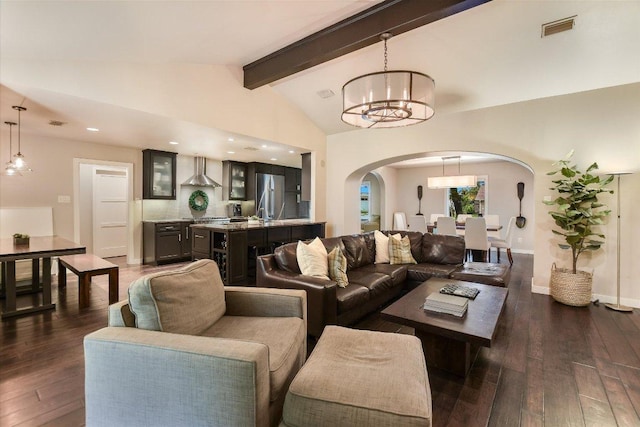 living area with visible vents, an inviting chandelier, lofted ceiling with beams, dark wood-style floors, and arched walkways