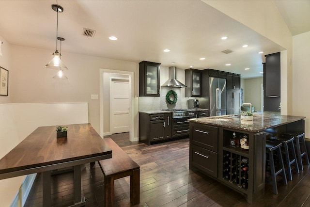 kitchen featuring wall chimney range hood, a kitchen breakfast bar, stainless steel appliances, and dark wood finished floors
