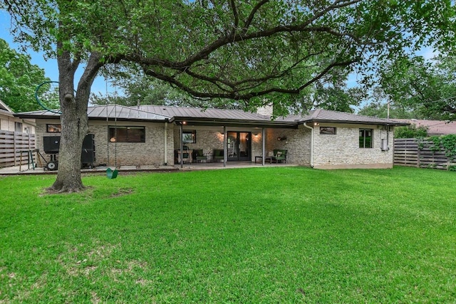 back of house featuring a standing seam roof, metal roof, a yard, a patio, and stone siding