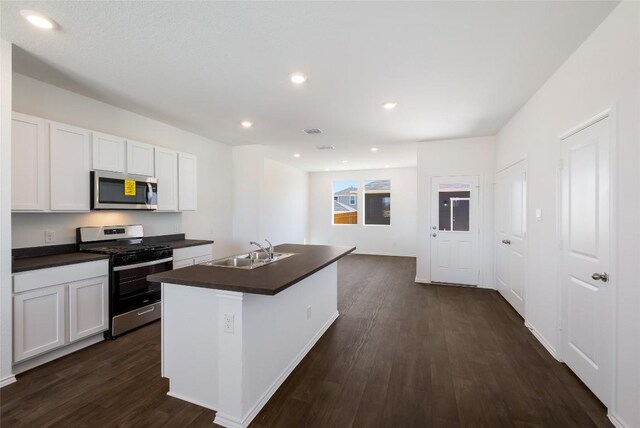 kitchen with dark countertops, an island with sink, dark wood-type flooring, a sink, and stainless steel appliances