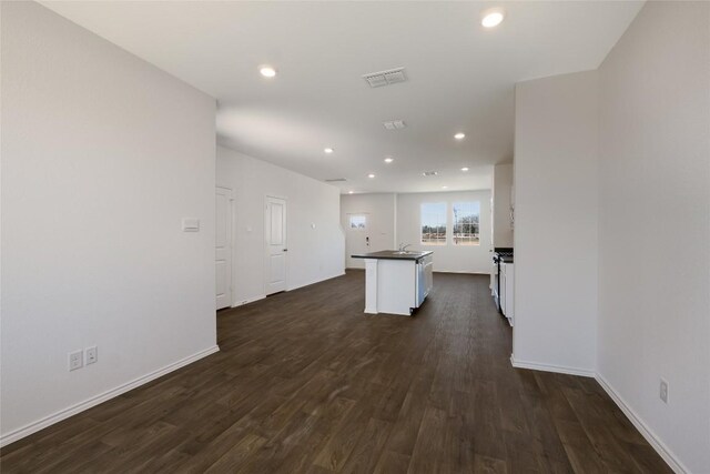 interior space with dark countertops, a center island with sink, recessed lighting, visible vents, and dark wood-style floors