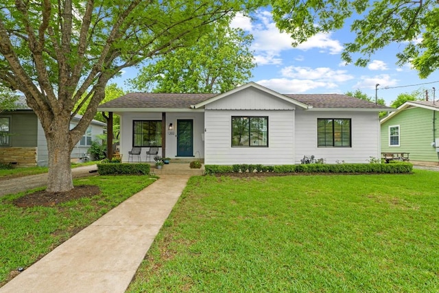 ranch-style house featuring roof with shingles, covered porch, and a front yard