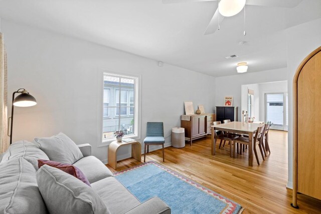 living area featuring ceiling fan, baseboards, and light wood-style floors