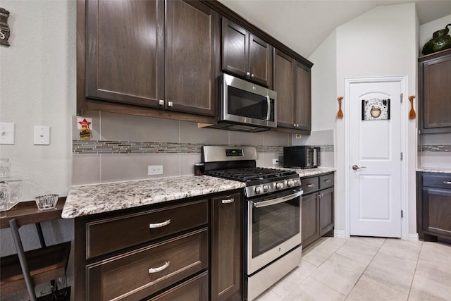 kitchen featuring dark brown cabinetry, appliances with stainless steel finishes, light stone countertops, light tile patterned floors, and lofted ceiling