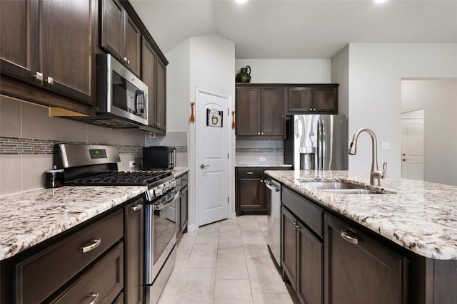 kitchen with light stone countertops, dark brown cabinets, tasteful backsplash, a sink, and stainless steel appliances