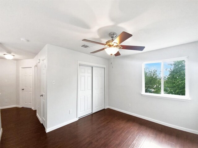 unfurnished bedroom with visible vents, baseboards, dark wood-style floors, and a closet