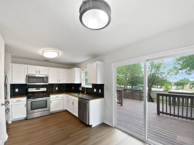 kitchen with dark countertops, appliances with stainless steel finishes, a sink, decorative backsplash, and wood finished floors