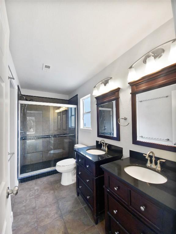 full bathroom with toilet, two vanities, a sink, and a stall shower