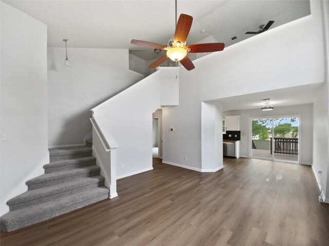 unfurnished living room featuring a ceiling fan, stairs, wood finished floors, and a towering ceiling