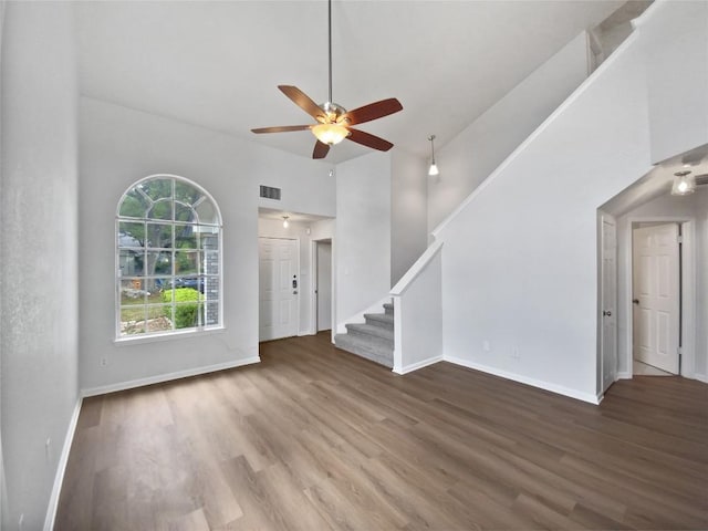 unfurnished living room featuring a ceiling fan, visible vents, wood finished floors, and a towering ceiling
